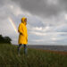 Man in yellow raincoat with hood walk on the beach in rainy weat - Meteo: esiste la maledizione dei fine settimana?