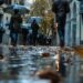 Blur obscures faces as people walk by with rain gear and leaves litter the wet - Le stupefacenti conseguenze meteo del blocco Rex