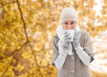 Woman in warm clothing holding mugs against tranquil autumn scene in forest - Temperature folli! Autunno pieno a 30 gradi