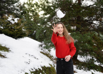 A young woman throws a snowball at the camera against the background of Christmas trees, winter activity and fun. new year and holidays concept - Meteo Islanda: +21.4°C a mezzanotte! Rischio di frane, venti forti e caldo estivo anomalo