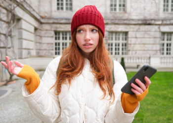 Portrait of confused girl tourist with smartphone, shrugs puzzled, dont know where to go, holds mobile phone with map application - Il Mediterraneo troppo caldo, un incubo per i fenomeni meteo estremi