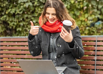 Young woman working on laptop sitting on a park bench with coffee. Computer and online shopping use. Distance learning, online education. - Ecco la data che segna la fine dell’anticiclone meteorologico