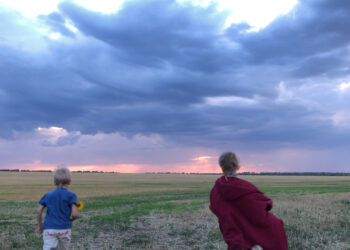 Two children run across a field against the background of clouds at sunset.A boy and a girl in a field against the background of storm clouds - Meteo: freddo notturno, ci prepariamo per le prime gelate