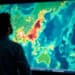 Man analyzing global heatmap climate change global warming data visualization large screen display science technology research environment geography cartography silhouette weather patterns world map - Meteo: Temperature costantemente sopra la media, ma in calo graduale