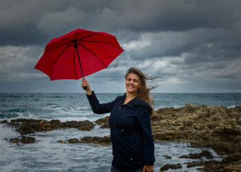 Young woman with a red umbrella on the background of the sea - Meteo: neve a bassa quota, inizio d’inverno bianco in molte regioni