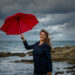 Young woman with a red umbrella on the background of the sea - Bomba del vortice polare: sorprendenti sorprese meteo in arrivo