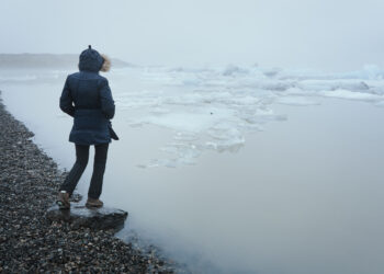 Person sitting on a rock by a lake with ice and surrounded by fog in winter. Jokulsarlon Glacial Lake - Artico o Nord Atlantico? Il dilemma meteo di inizio dicembre