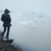 Person sitting on a rock by a lake with ice and surrounded by fog in winter. Jokulsarlon Glacial Lake - Meteo: Sabato 30 novembre, freddo, pioggia e neve in queste regioni