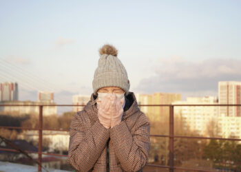 Woman in a medical mask in the setting sun on the street sneezes covering her mouth with her hands. coronovirus, covid-19 - L’autunno ci saluterà con un meteo da pieno inverno