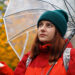 Young girl in warm clothes with a transparent umbrella and a backpack on her back outside in cold weather after rain. Woman looks at the camera. - Meteo: un bolide pieno di freddo e neve trafigge l’anticiclone