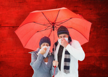 Mature couple blowing their noses under umbrella against red wooden planks - Meteo: continua a piovere, ecco quando arriverà il freddo