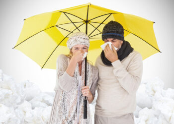 Couple sneezing in tissue while standing under umbrella against white background with vignette - Meteo: il clima sarà meno freddo nei prossimi giorni, durerà?