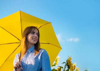 Young woman in dress and yellow umbrella on a field of sunflower - Chiedere un inverno meteorologicamente normale è troppo? No, è giusto