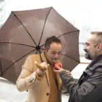 An executive offers a red apple to another who sucks it under the umbrella on a rainy day - Previsioni meteo: forti piogge nelle prossime sei giorni in queste regioni