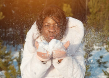 dark-skinned woman in a white coat holds snow in her hands and wants to blow it away - Meteo del weekend: fine del freddo, l’inverno è stato cacciato