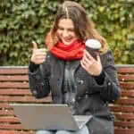 Young woman working on laptop sitting on a park bench with coffee. Computer and online shopping use. Distance learning, online education. - Meteo, tutto è possibile: da +19°C con Garbino a -13°C con Buran