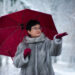 woman in a gray fur coat with a red umbrella stands on a white, snow-covered background. - Meteo: il ruggito dell’inverno