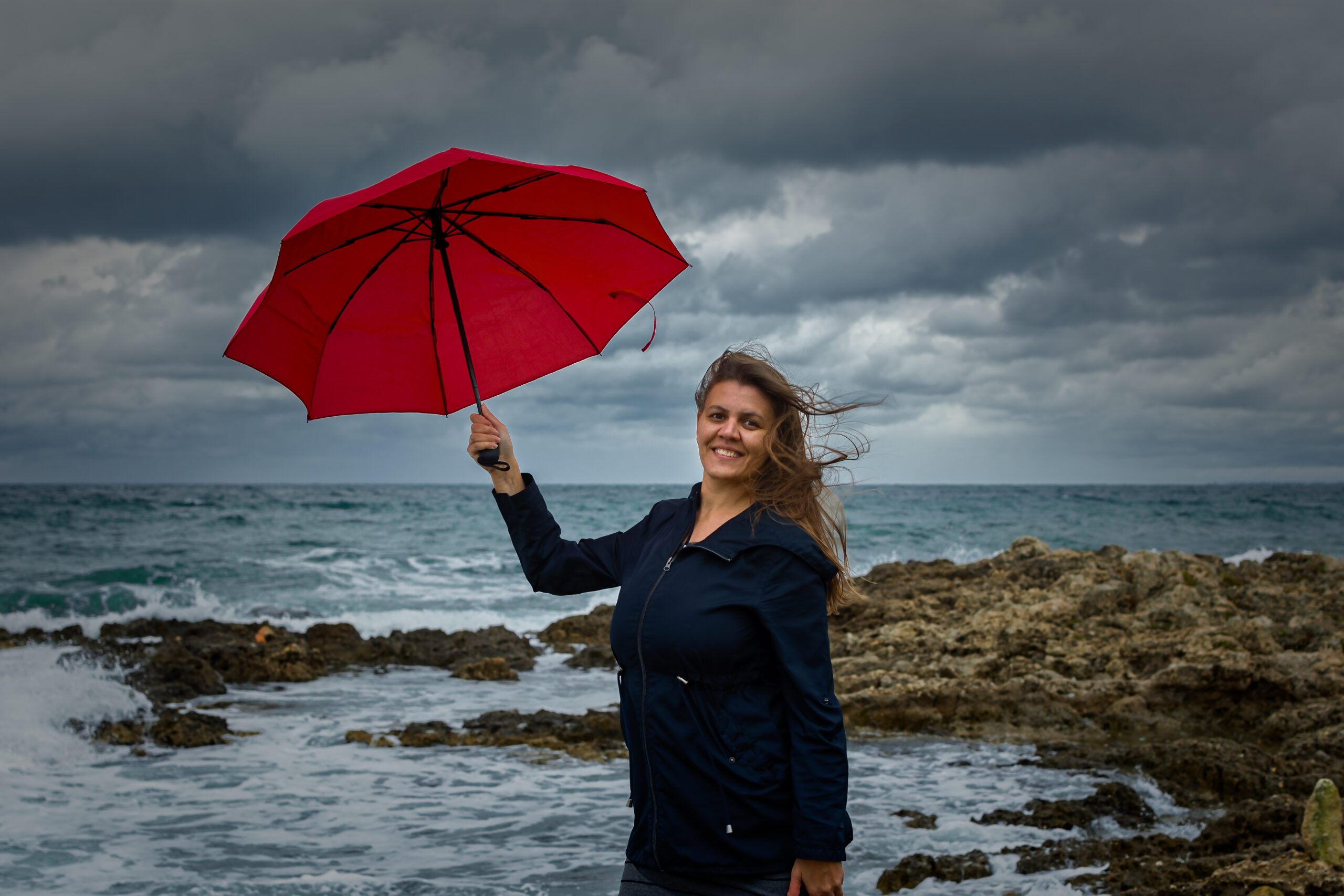 Young woman with a red umbrella on the background of the sea - Meteo: weekend perturbato, ecco dove servirà l’ombrello