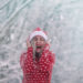 Cheerful woman enjoys winter wonderland. Snow flies on her and she is happy, rejoices cold weather. Girl in red Christmas sweater and Santa hat. - Meteo: Dicembre invernale, previsti ulteriori freddo e neve