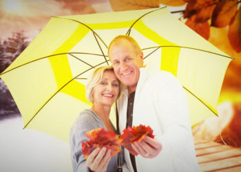 Happy mature couple showing autumn leaves under umbrella against autumn changing to winter - Paradosso meteo: alta pressione ma cielo grigio e pioggia