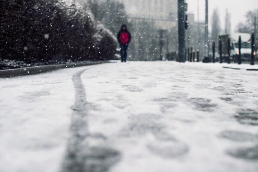 Low angle shot of a person walking on the snow covered sidewalk under the snow - Pioggia tra 6 e 7 Gennaio, ombrelli aperti su queste regioni